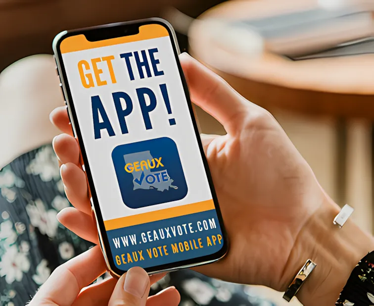Person holding a smartphone displaying a promotional screen for the Geaux Vote mobile app, featuring Louisiana's outline with a checkmark and the text ‘GEAUX VOTE’, along with a website URL and call-to-action to download the app.